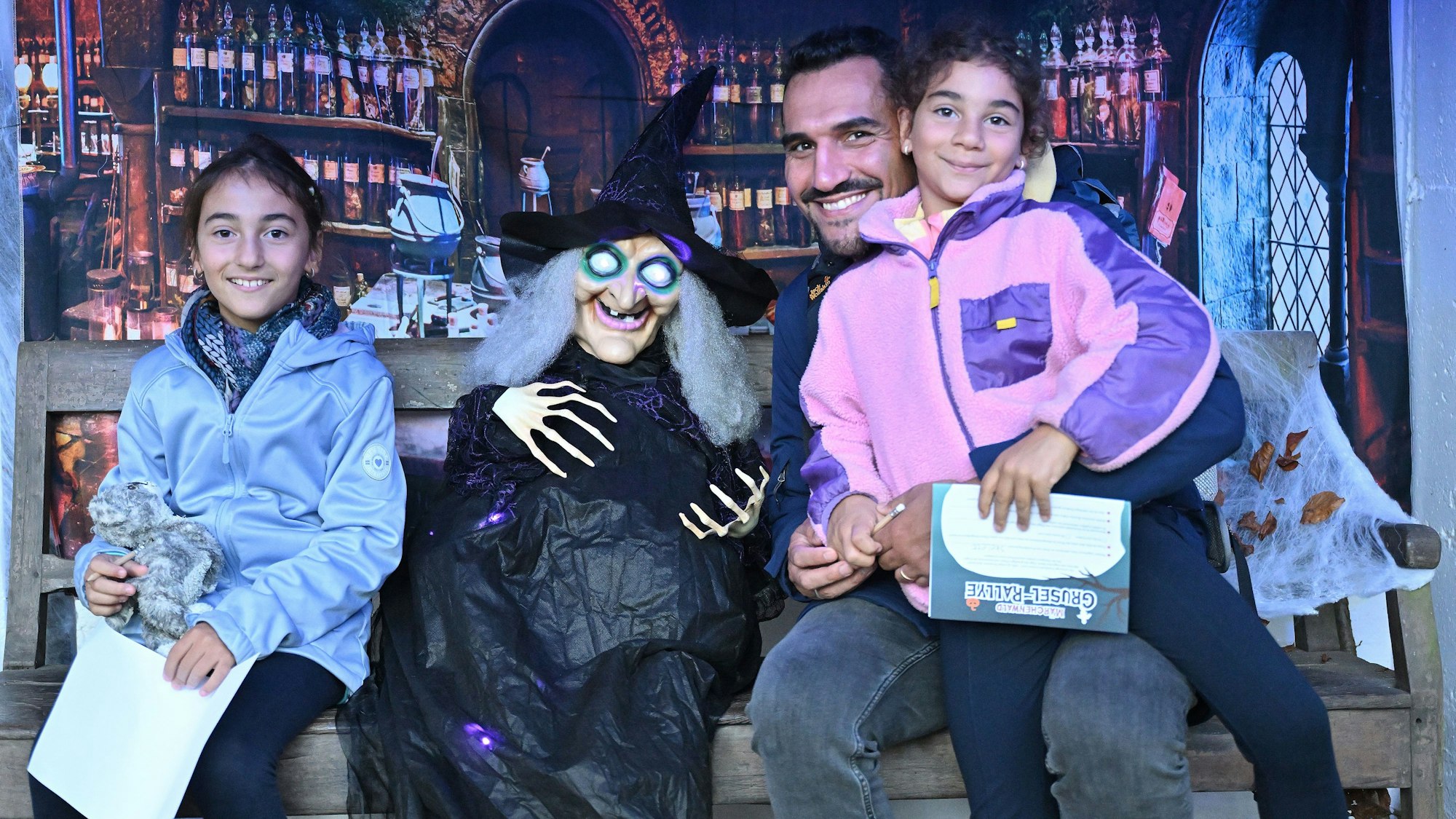 Eine Familie sitzt mit einer Hexe auf einer Bank im Altenberger Märchenwald.