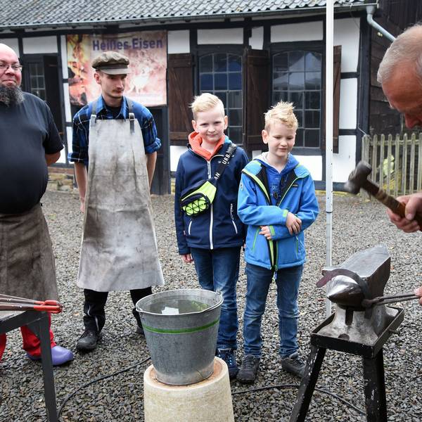 Am Amboss zeigt ein Schmiedemeister, wie mit vielen Hammerschlägen ein Hufeisen entsteht.