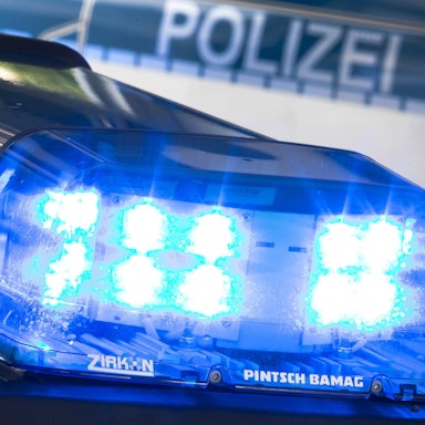 Ein Blaulicht leuchtet auf dem Dach eines Polizeiwagens. Im Hintergrund steht ein weiterer Streifenwagen.