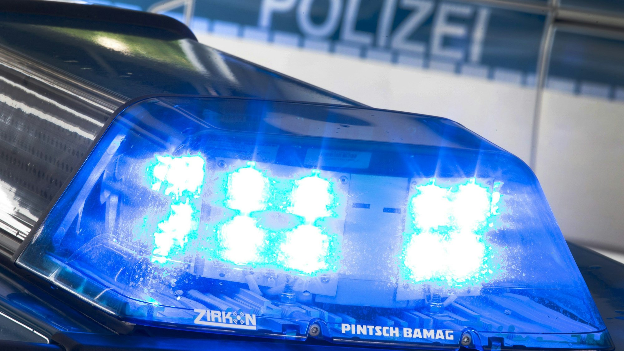 Ein Blaulicht leuchtet auf dem Dach eines Polizeiwagens. Im Hintergrund steht ein weiterer Streifenwagen.