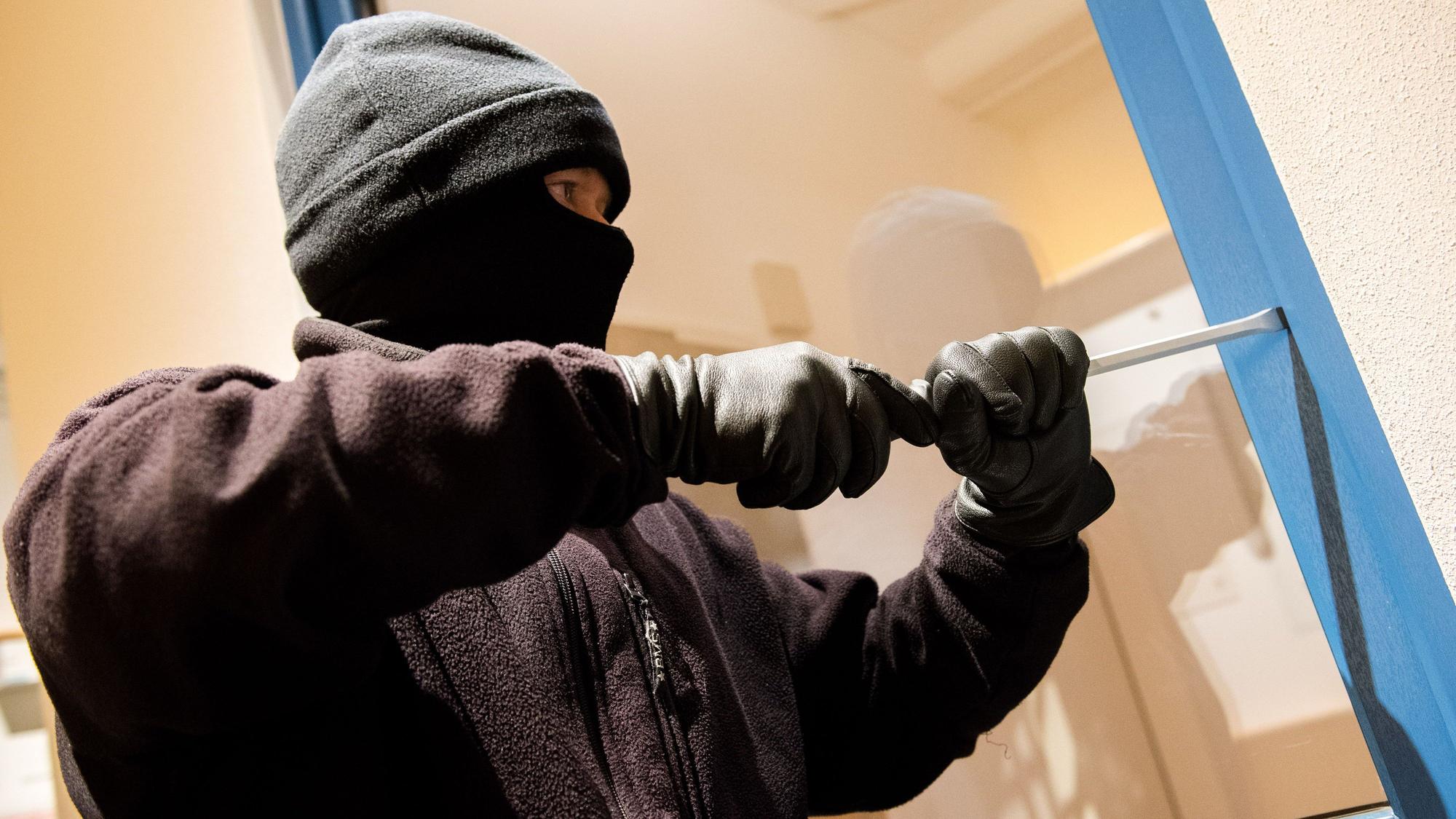 Ein als Einbrecher verkleideter Mann hebelt ein Fenster auf.
