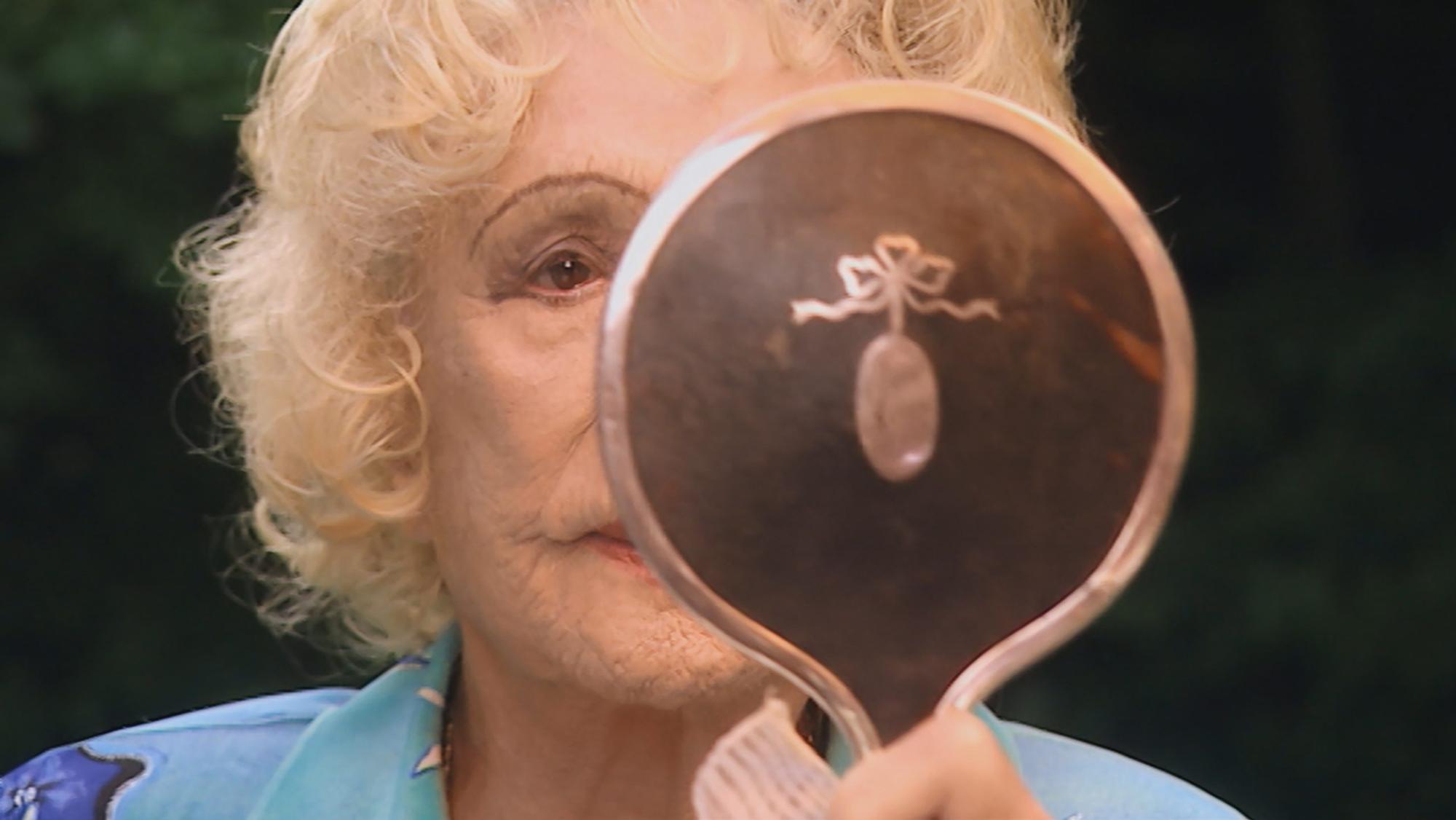 Leni Riefenstahl blickt in einen Handspiegel.