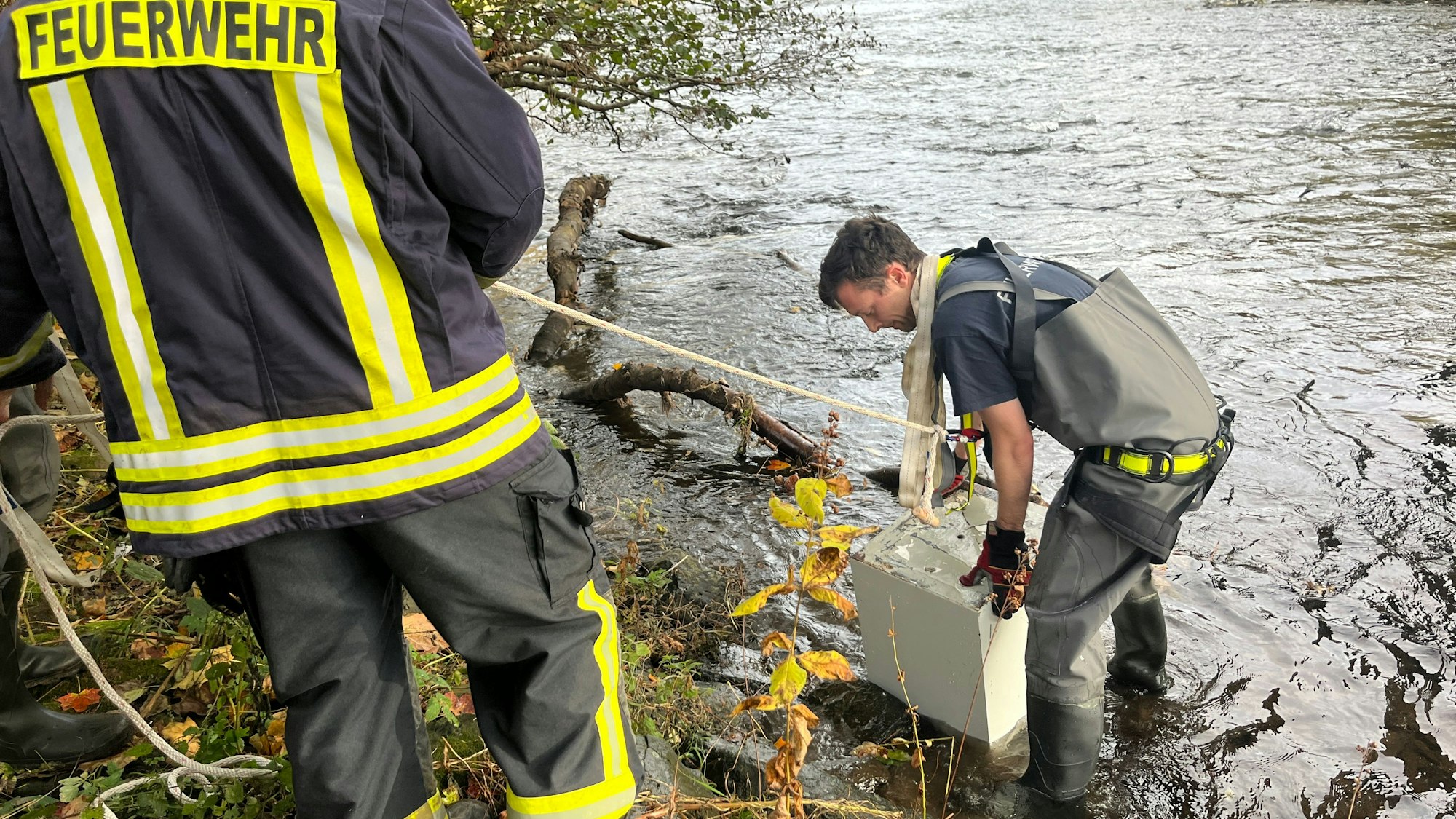 Ein Feuerwehrmann hebt einen Tresor aus dem Wasser.