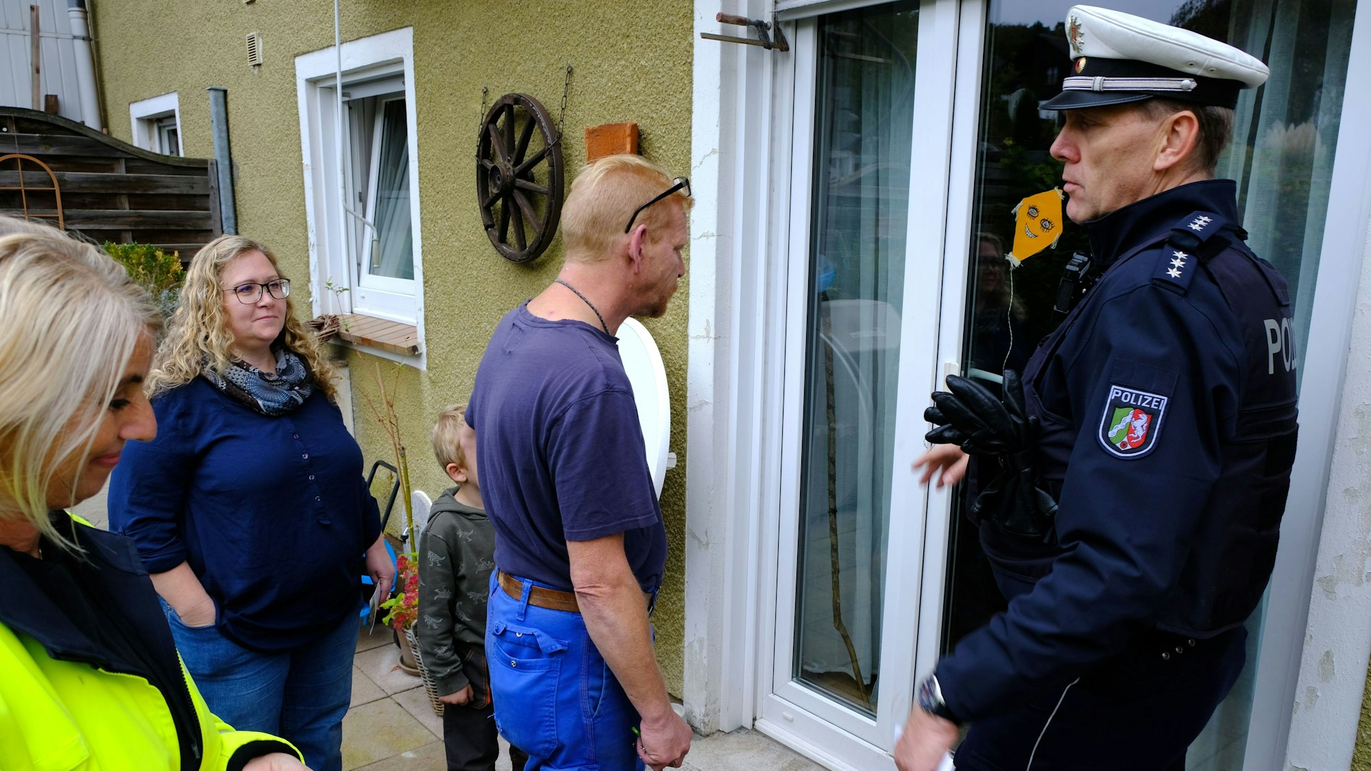 Der Polizist und die Beraterin stehen mit einer Familie im Freien vor einer Terrassentür.