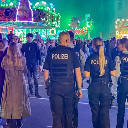 Das Bild zeigt vier Polizeibeamte, die über den Kirmesparcours gehen.