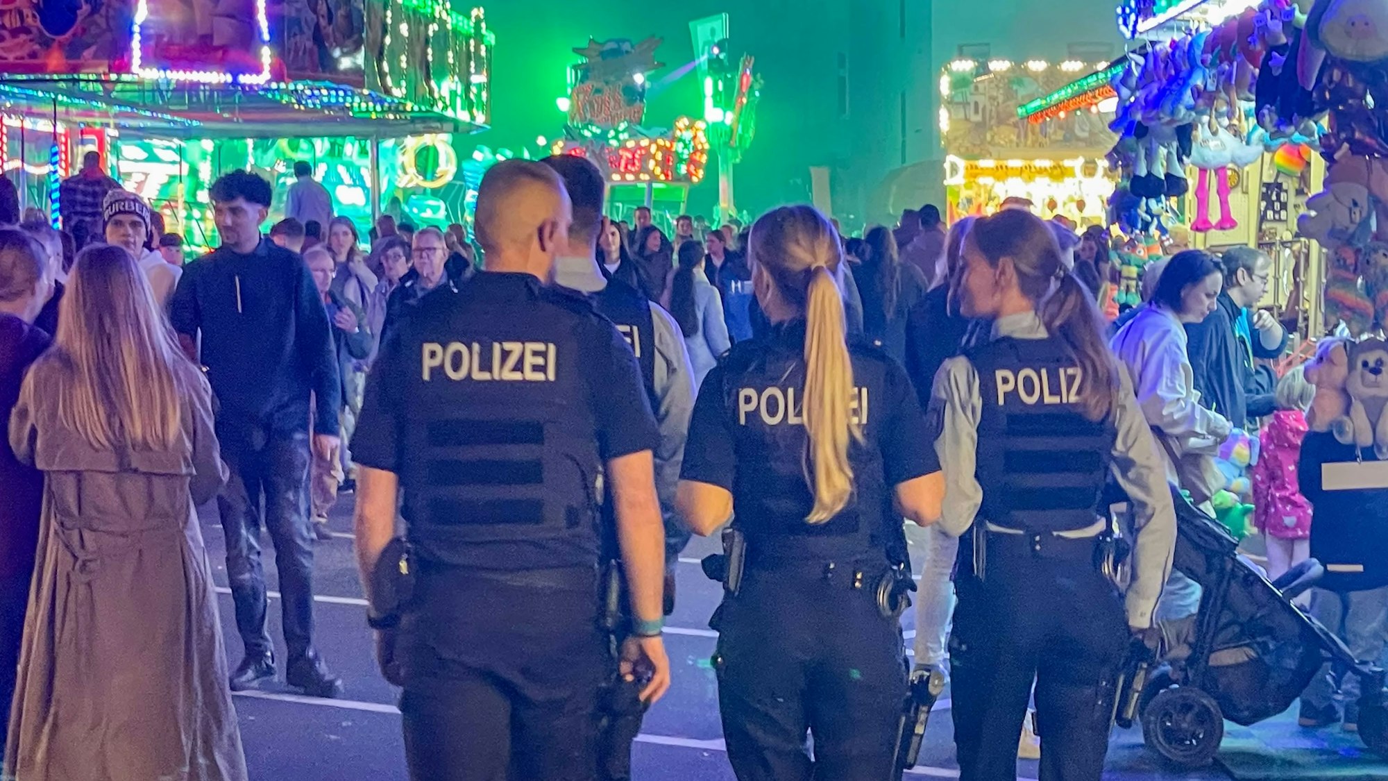 Das Bild zeigt vier Polizeibeamte, die über den Kirmesparcours gehen.