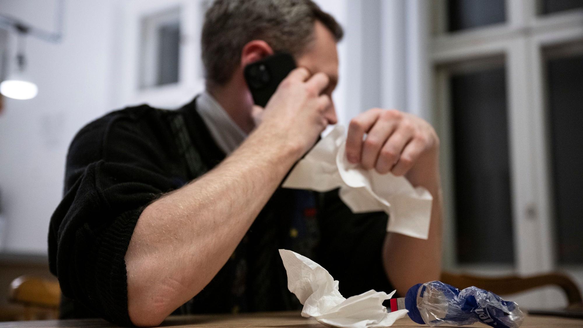 Ein Mann hält ein Taschentuch in einer Hand und ein Telefon in der Anderen. (Symbolbild)