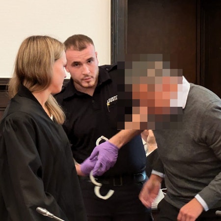 Dem ehemaligen Geschäftsführer werden von einem Justizbeamten die Handfesseln abgenommen.