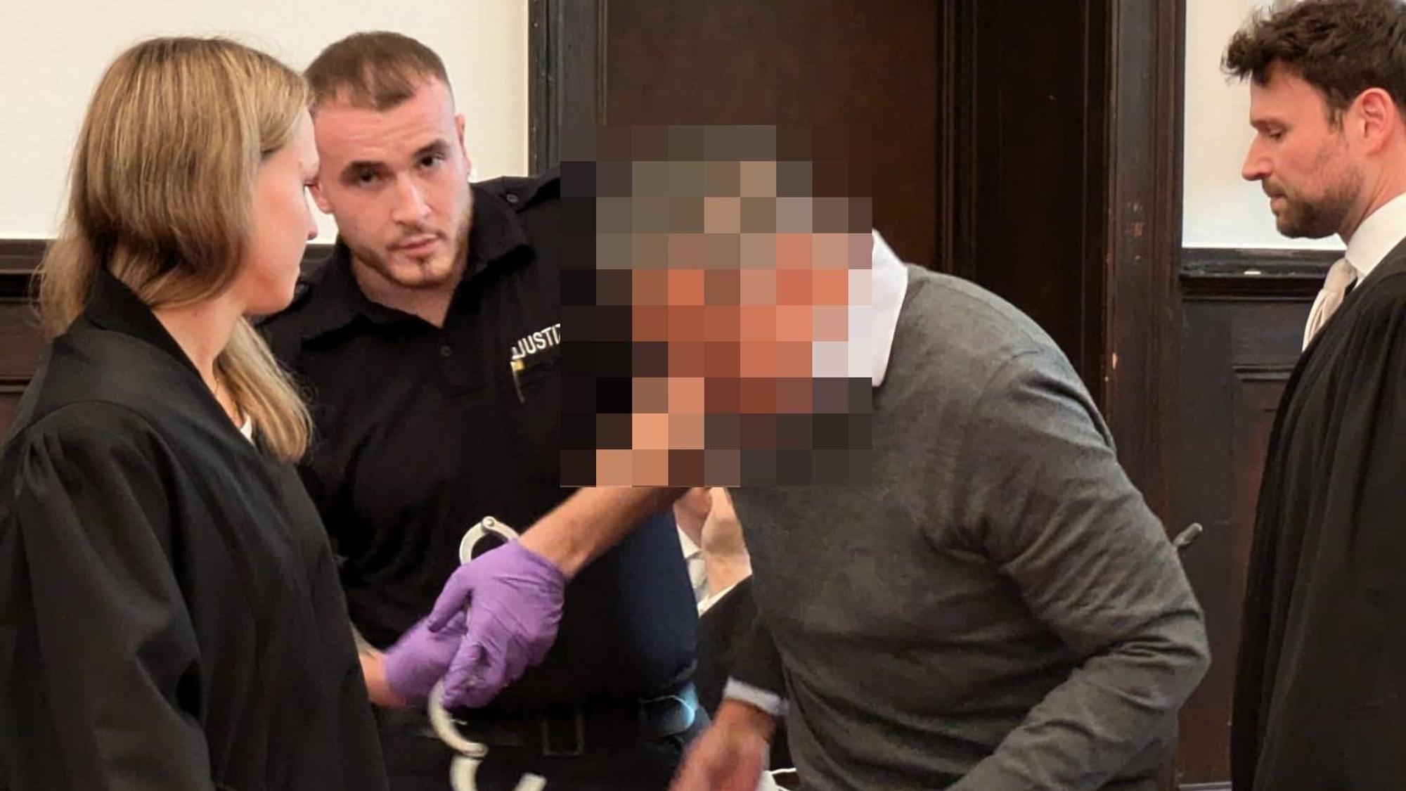 Dem ehemaligen Geschäftsführer werden von einem Justizbeamten die Handfesseln abgenommen.