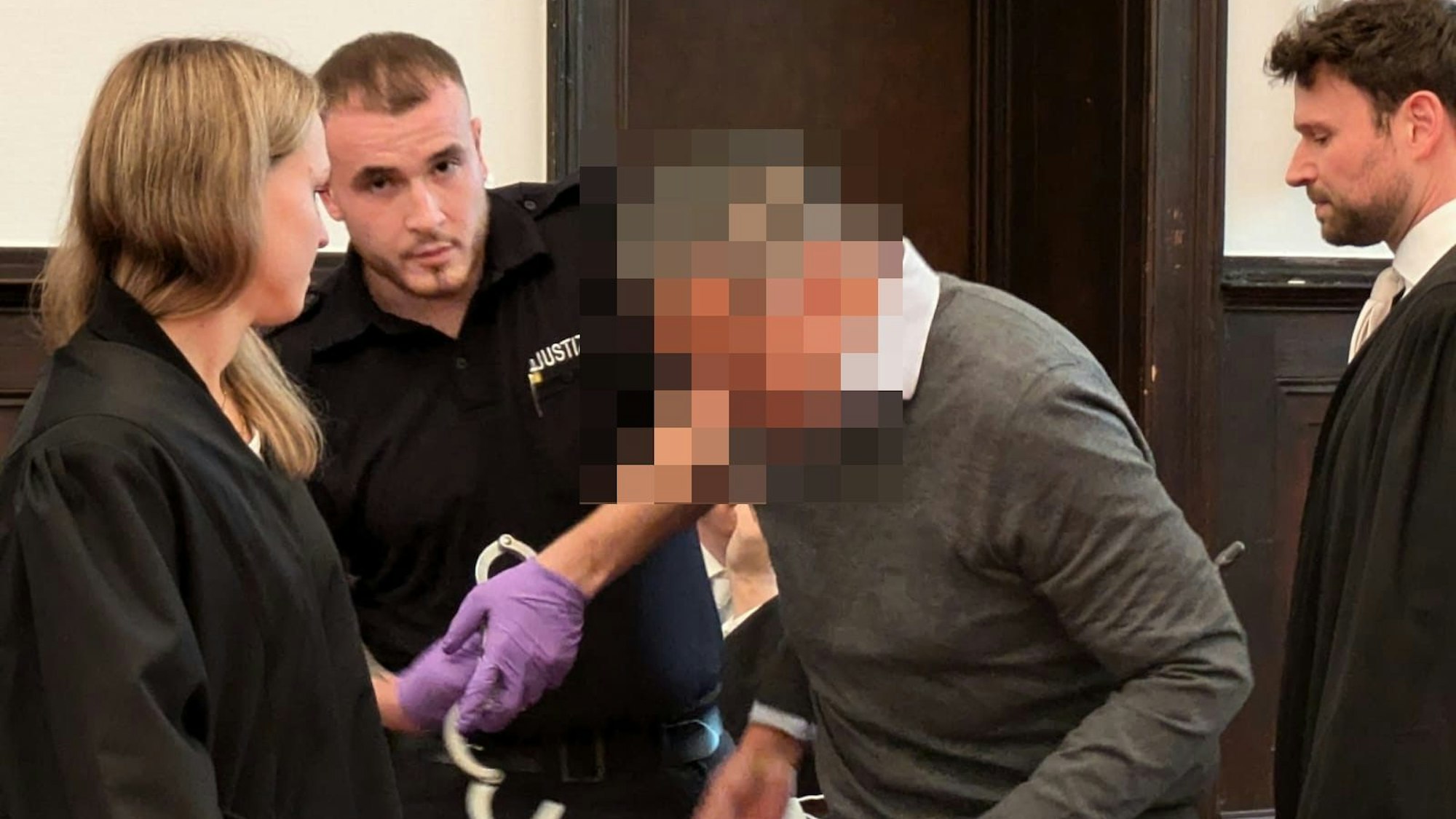 Dem ehemaligen Geschäftsführer werden von einem Justizbeamten die Handfesseln abgenommen.