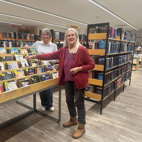 Zwei Frauen stehen an einem Bücherregal in einer Bücherei.