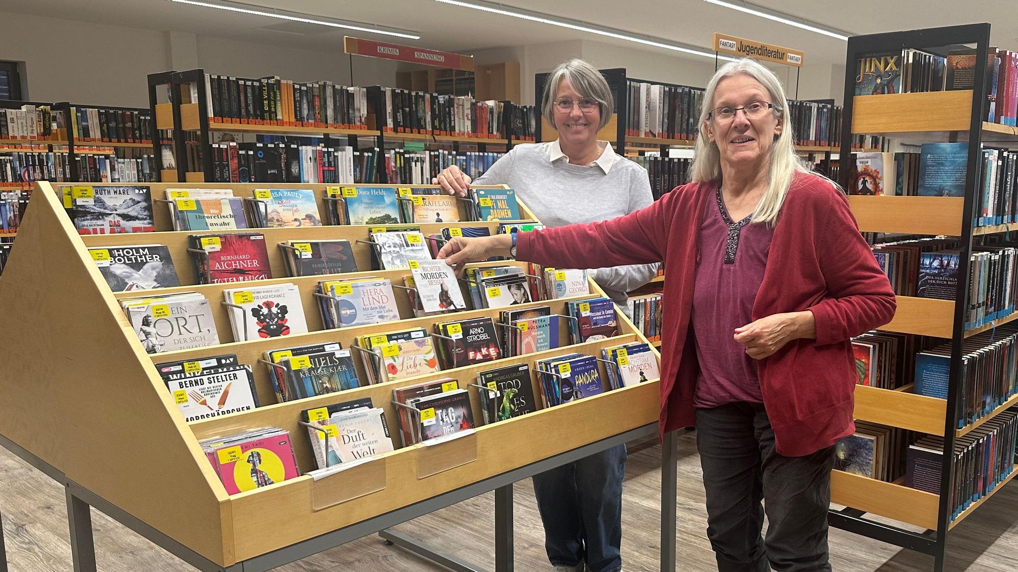 Zwei Frauen stehen an einem Bücherregal in einer Bücherei.
