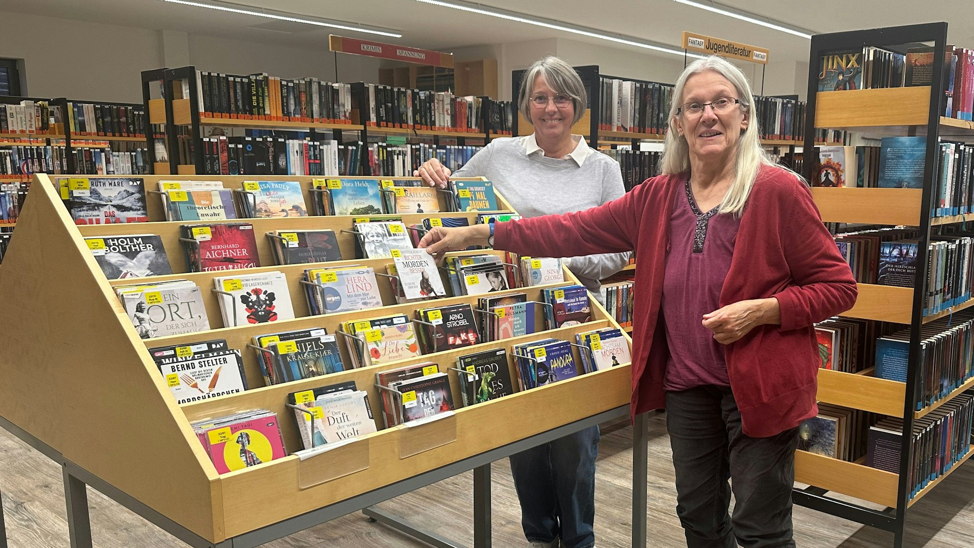 Zwei Frauen stehen an einem Bücherregal in einer Bücherei.