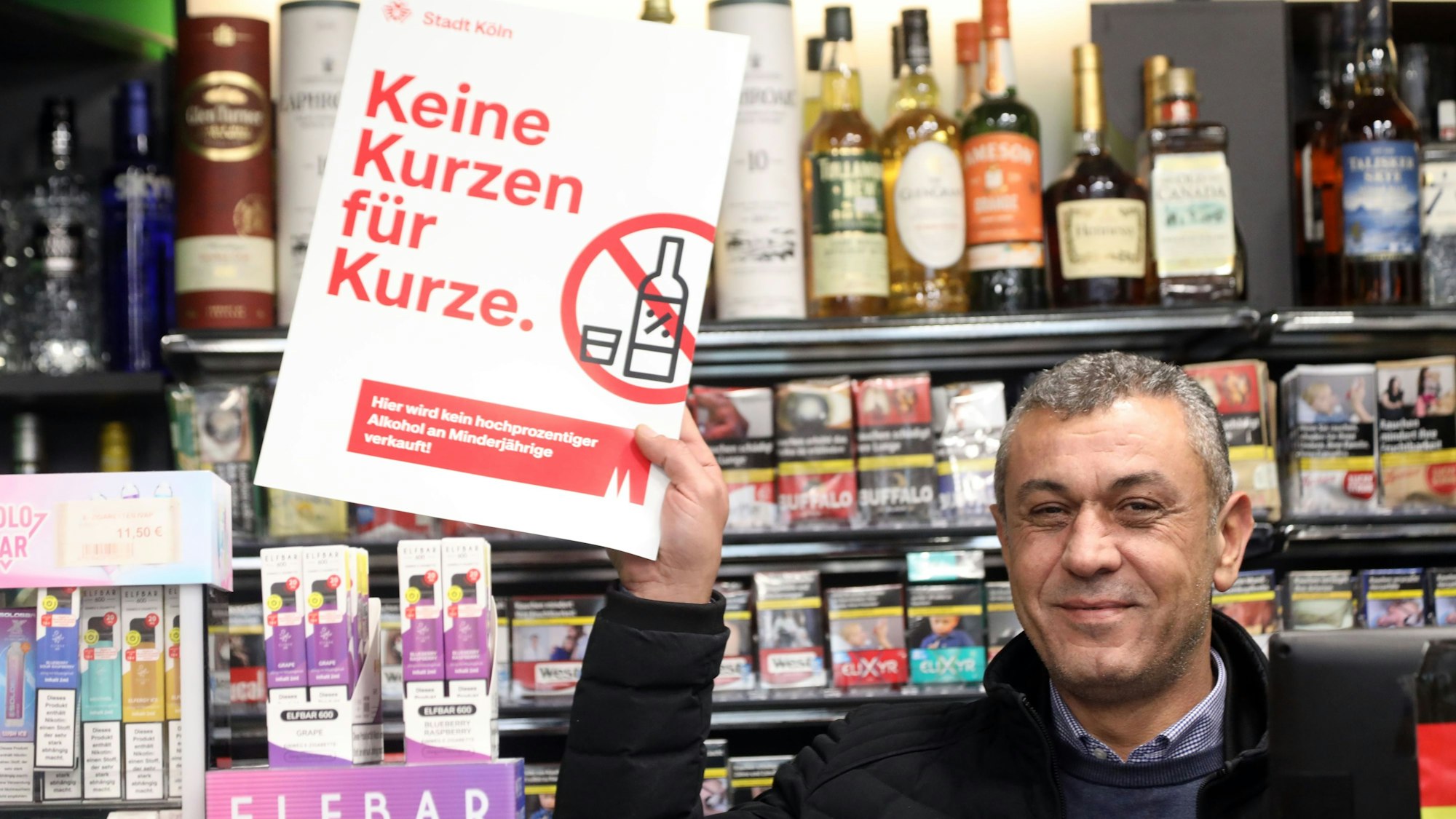 Verkäufer Kenan Aslan zeigt in einem Kiosk an der Marzellenstraße ein Plakat mit dem bekannten Motto „Keine Kurze für Kurze“'.