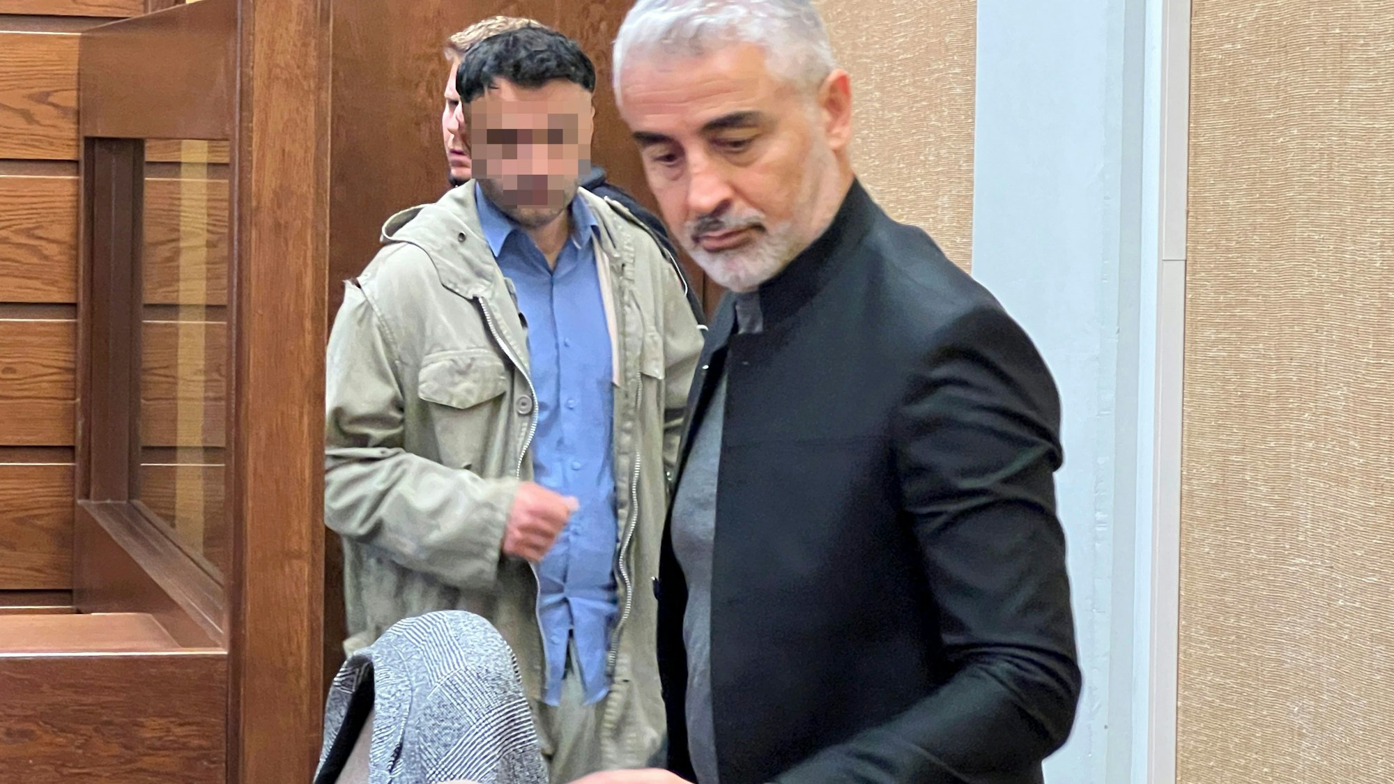 Landgericht Köln: Ein Mann soll einen anderen in Rheindorf mit fast 26 Messerstichen getötet haben. Hier wird er aus dem Keller in den Gerichtssaal geführt. Im Vordergrund: Verteidiger Mustafa Kaplan.