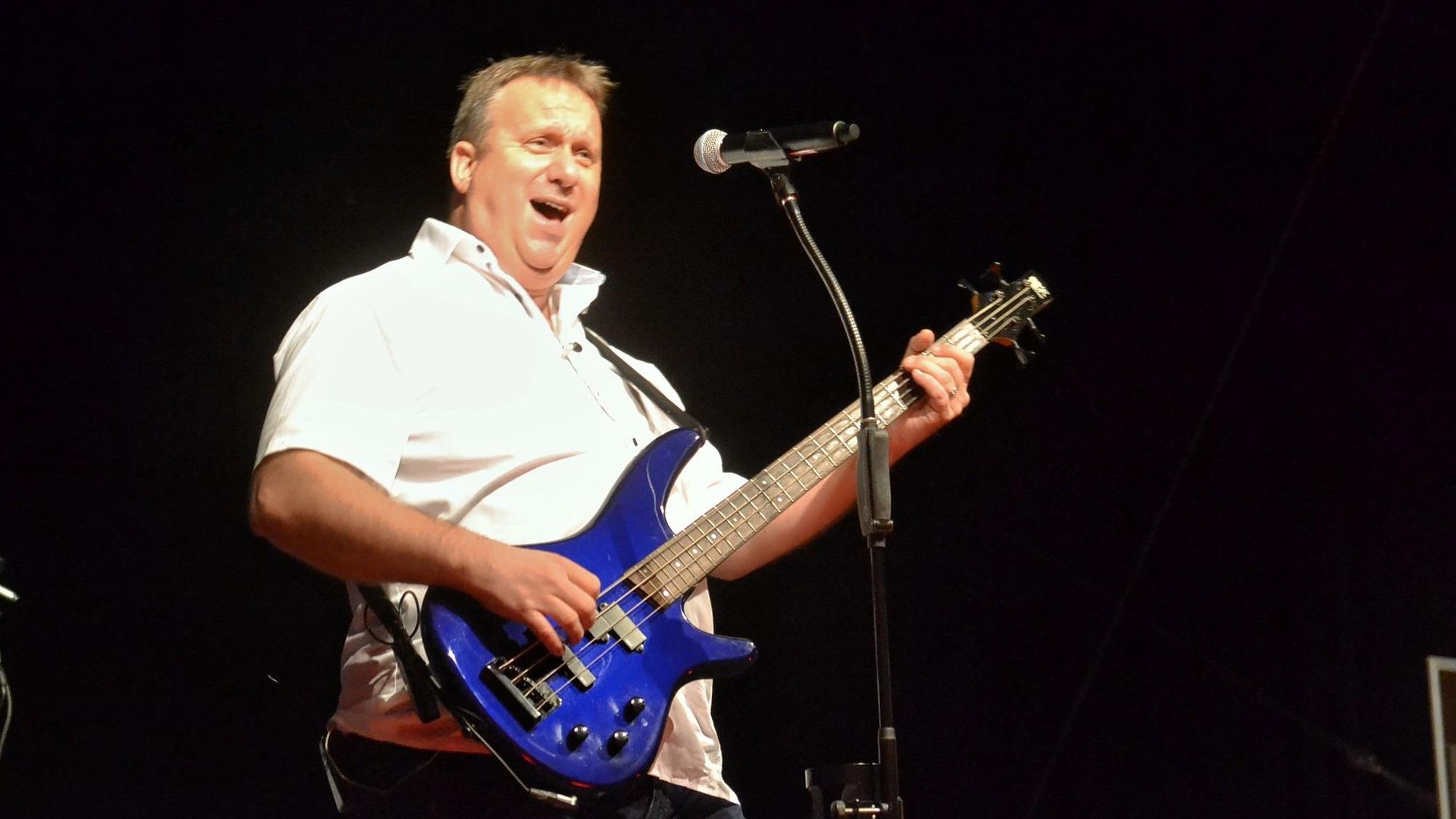 Ein Mann spielt auf einem blauen Bass und singt in ein Mikrofon.