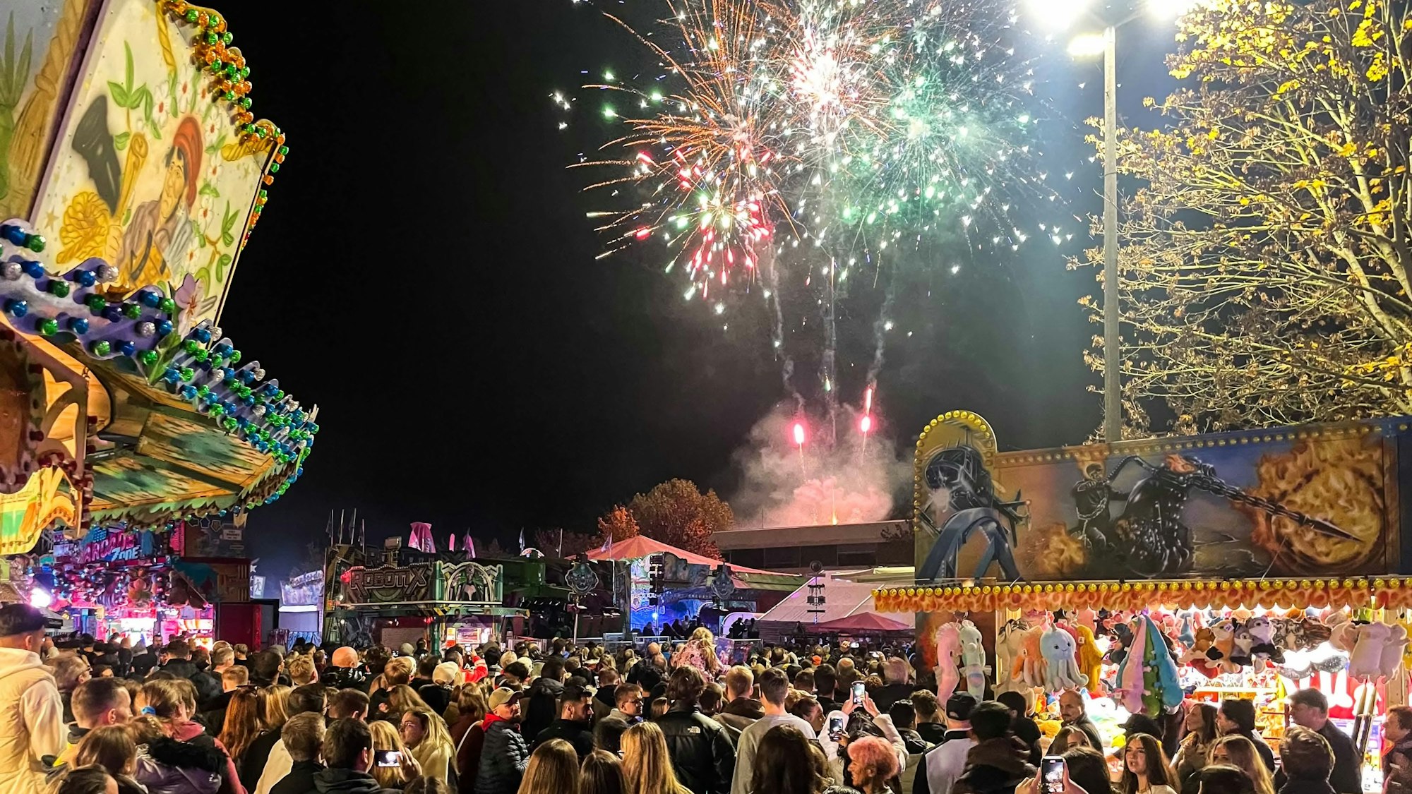 Das Bild zeigt das Feuerwerk über dem Charleviller Platz. Viele Menschen stehen auf dem Platz und schauen in den Himmel.