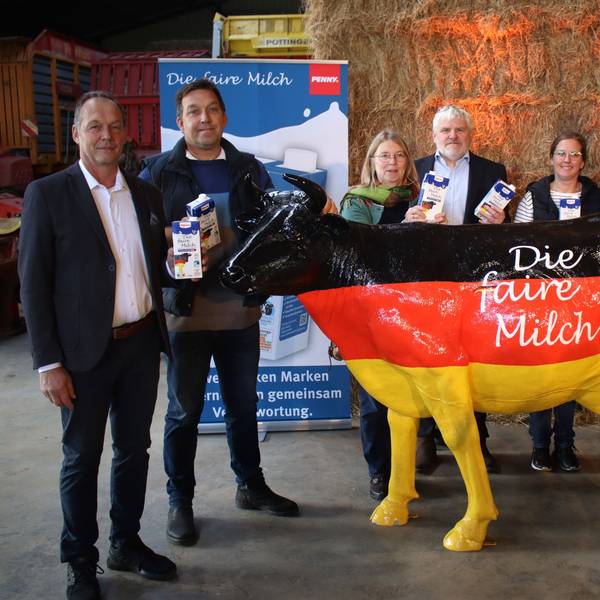 Die Vertragsunterzeichner stehen vor Strohballen und hinter einer schwarz-rot-goldenen Kuh. Einige halten Milchtüten in der Hand.