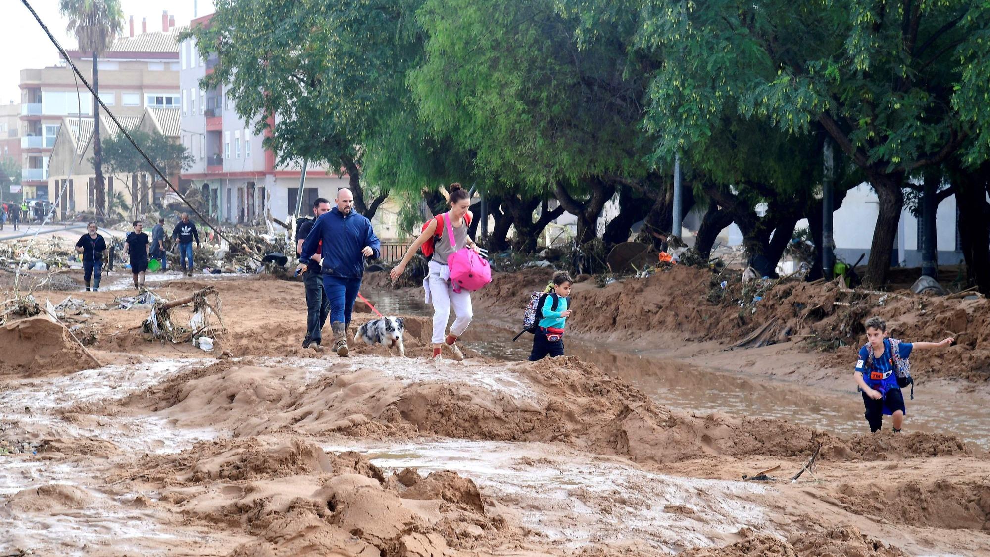 Family members walk in a street covered in mud in a flooded area in Picanya, near Valencia, eastern Spain, on October 30, 2024. Floods triggered by torrential rains in Spain's eastern Valencia region has left 51 people dead, rescue services said on October 30. (Photo by Jose Jordan / AFP)