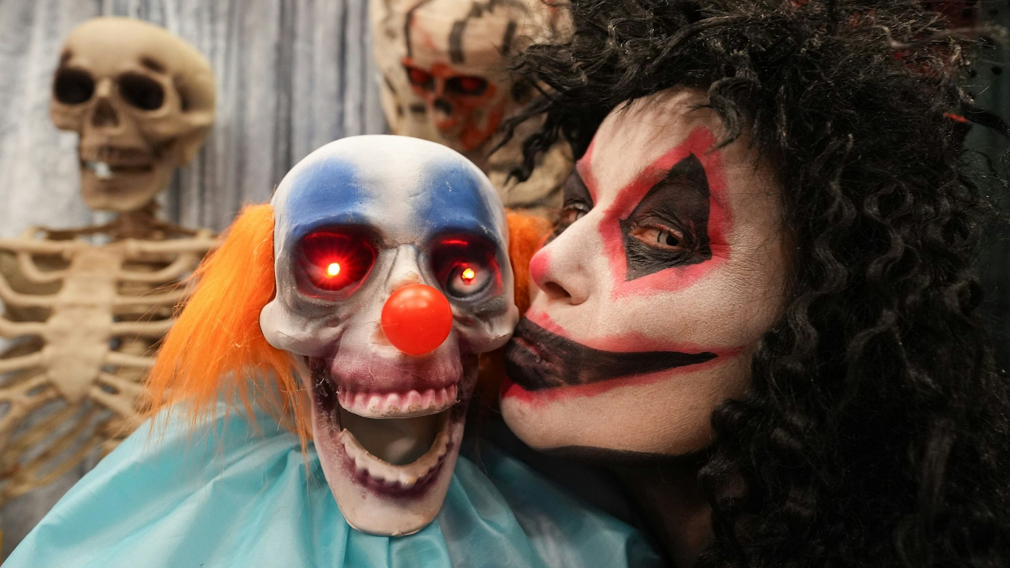 Die geschminkte und verkleidete Mitarbeiterin Simone Rumke küsst eine Grusel-Clownsfigur mit leuchtenden Augen.