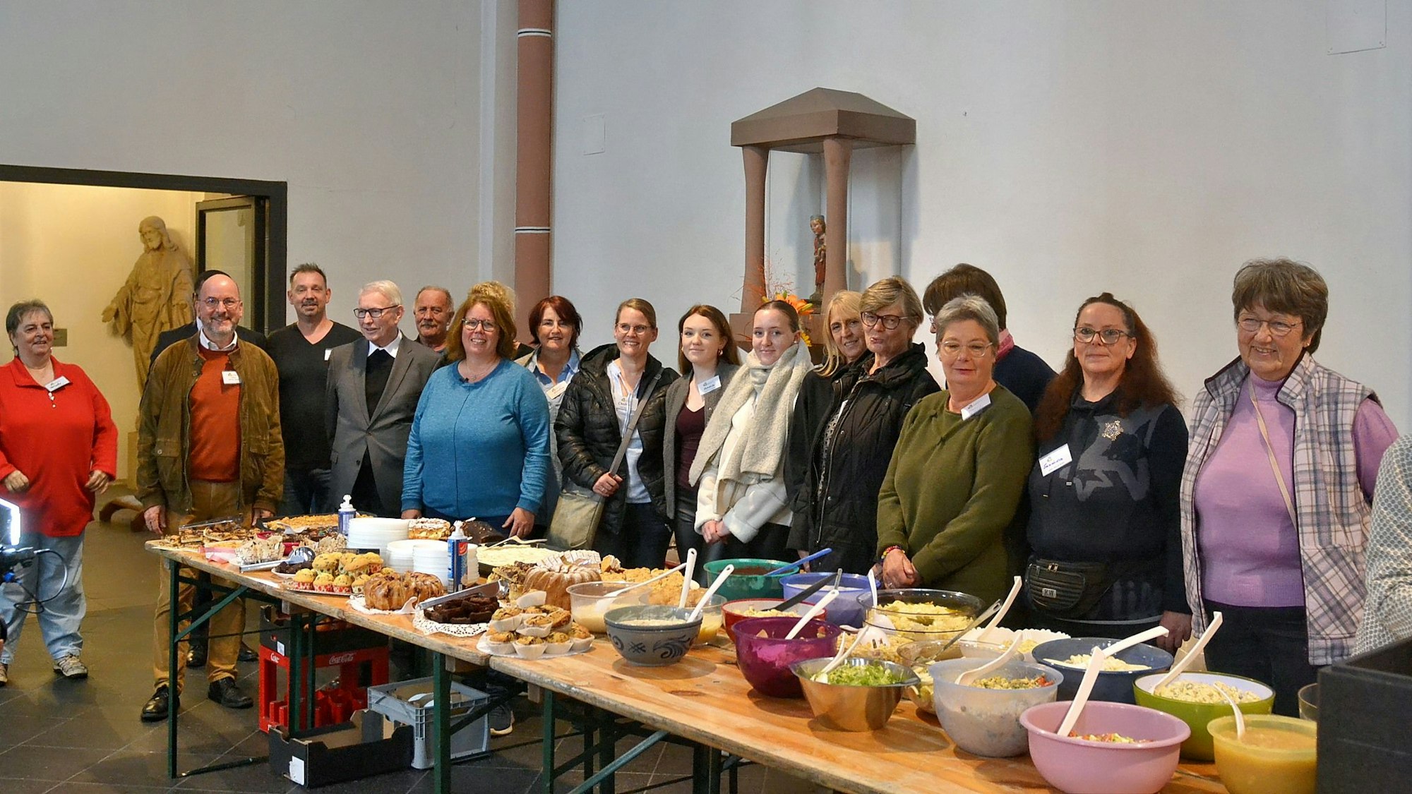 Zahlreiche Männer und Frauen stehen hinter einem langen Buffet-Tisch, auf dem viele Schüsseln mit Speisen stehen.