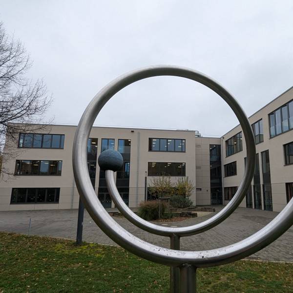 Das Foto zeigt eines der neuen Schulgebäude des Ernst-Mach-Gymnasiums hinter einem Sportgerät auf dem Schulhof.