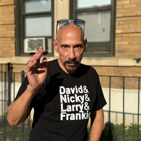 Nicky Siano grüßt in seiner Brooklyner Heimat. Er trägt ein schwarzes T-Shirt mit den Vornamen der New Yorker DJ-Pioniere David Mancuso, Nicky Siano, Larry Levan und Frankie Knuckles.