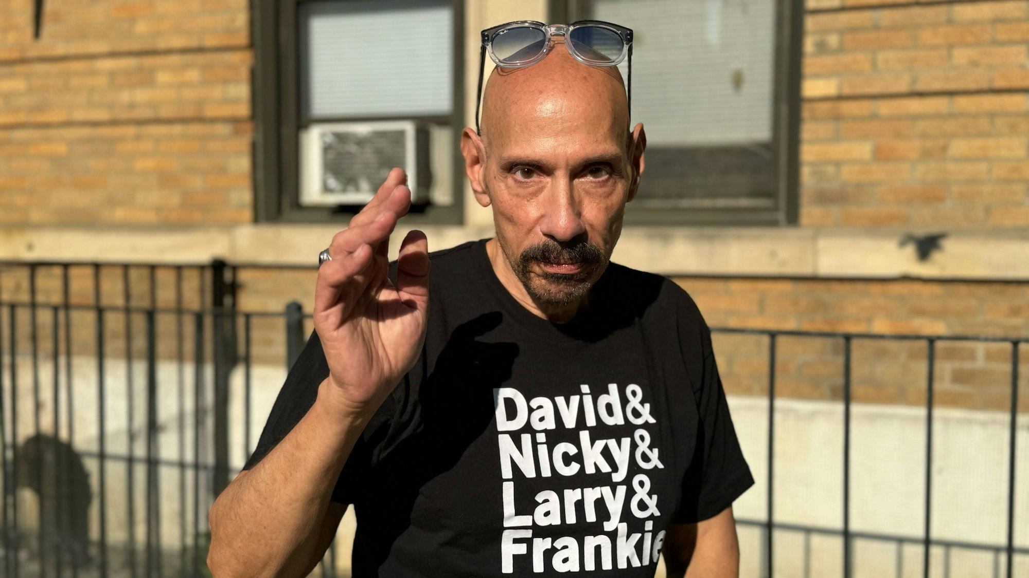 Nicky Siano grüßt in seiner Brooklyner Heimat. Er trägt ein schwarzes T-Shirt mit den Vornamen der New Yorker DJ-Pioniere David Mancuso, Nicky Siano, Larry Levan und Frankie Knuckles.