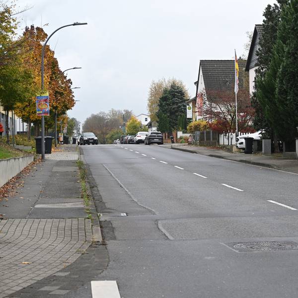 Man sieht den Gehweg sowie die Fahrbahn. Der Belag ist teilweise defekt.
