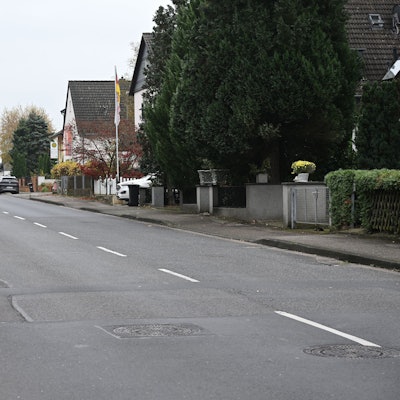 Man sieht den Gehweg sowie die Fahrbahn. Der Belag ist teilweise defekt.