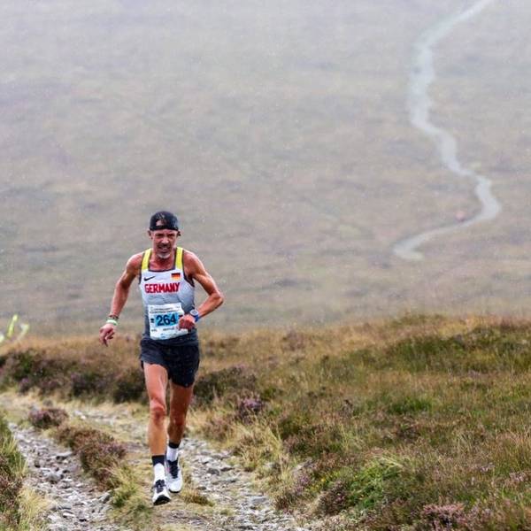 Ein Sportler mit umgekehrt aufgesetzter Kappe läuft über den grasigen Mittelstreifen eines Steinweges im Gebirge.