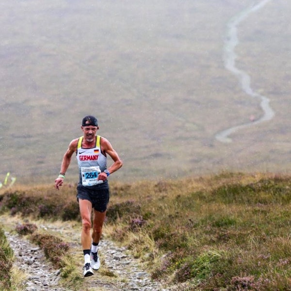 Ein Sportler mit umgekehrt aufgesetzter Kappe läuft über den grasigen Mittelstreifen eines Steinweges im Gebirge.