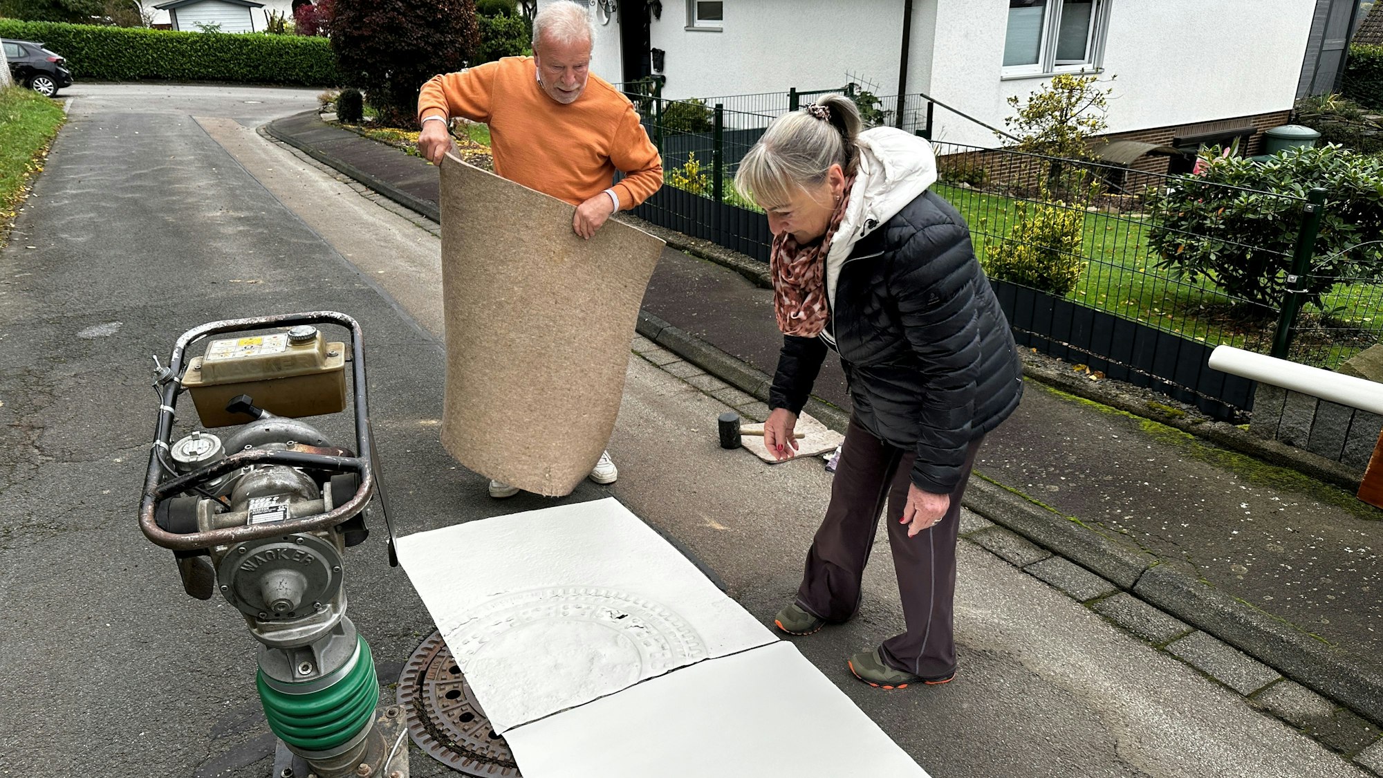 Ein Mann und eine Frau blicken auf ein Stück Papier, das vor ihnen auf der Straße liegt.