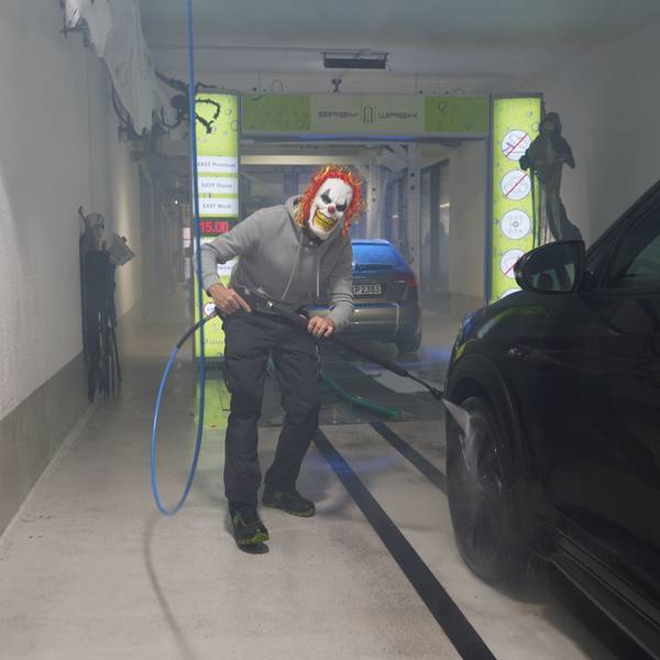 Das Foto zeigt einen Mann mit einer Clown-Maske, der ein Auto wäscht.
