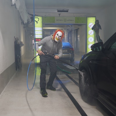 Das Foto zeigt einen Mann mit einer Clown-Maske, der ein Auto wäscht.