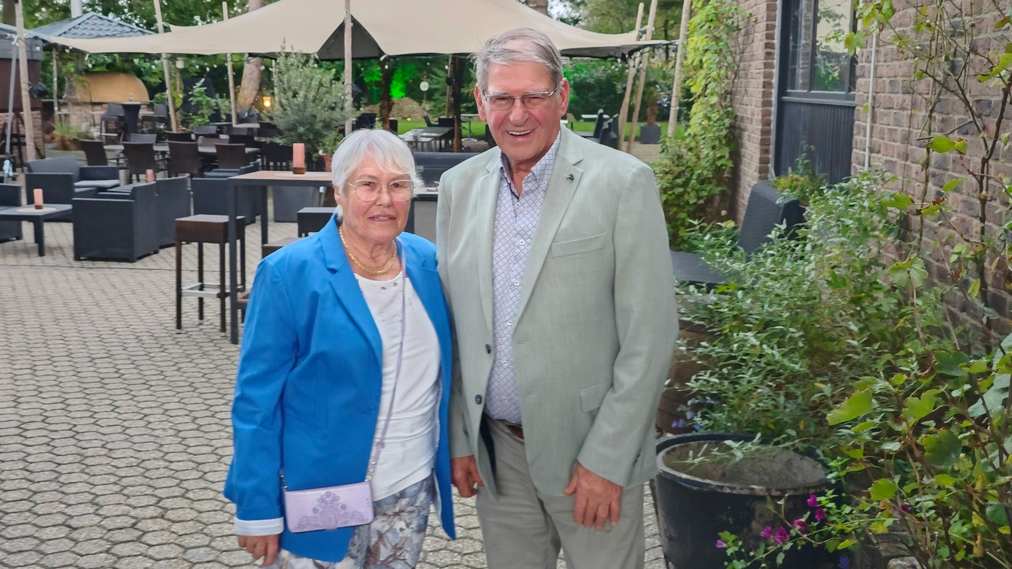 Die Eheleute stehen am Rand einer Restaurant-Terrasse und lächeln in die Kamera.