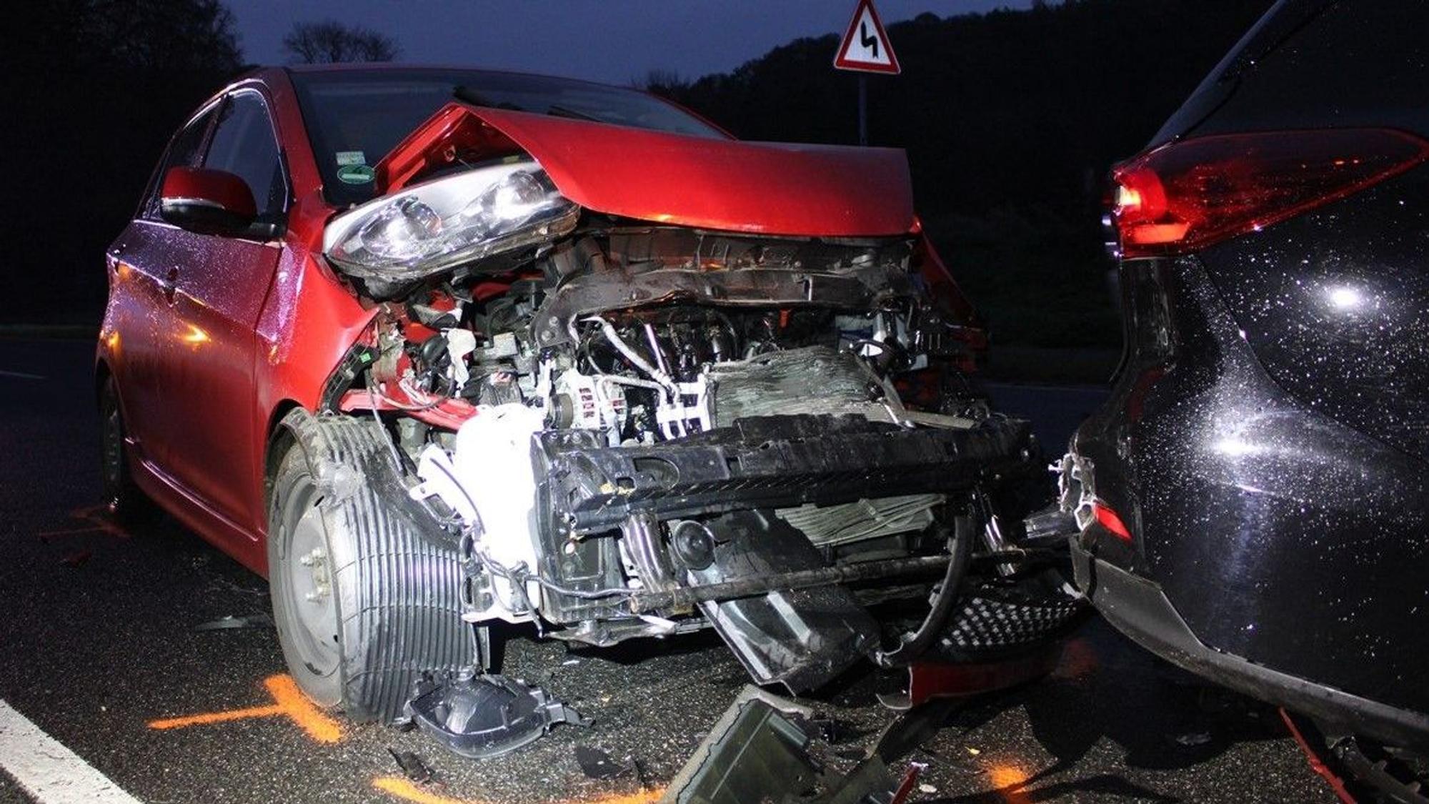 Ein schwer beschädigter roter Kia steht am Heck eines weiteren, ebenfalls beschädigten Fahrzeugs auf der Altenberger-Dom-Straße in Odenthal.