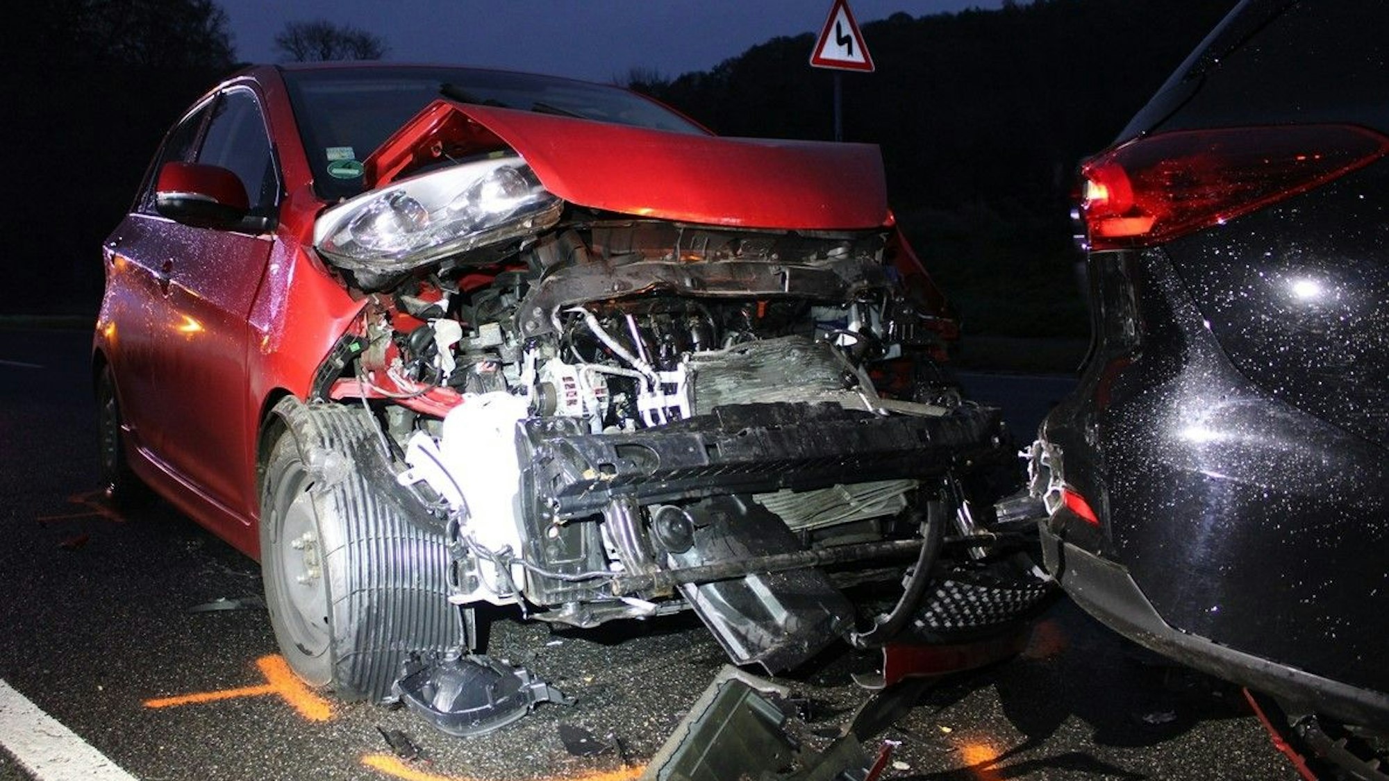 Ein schwer beschädigter roter Kia steht am Heck eines weiteren, ebenfalls beschädigten Fahrzeugs auf der Altenberger-Dom-Straße in Odenthal.