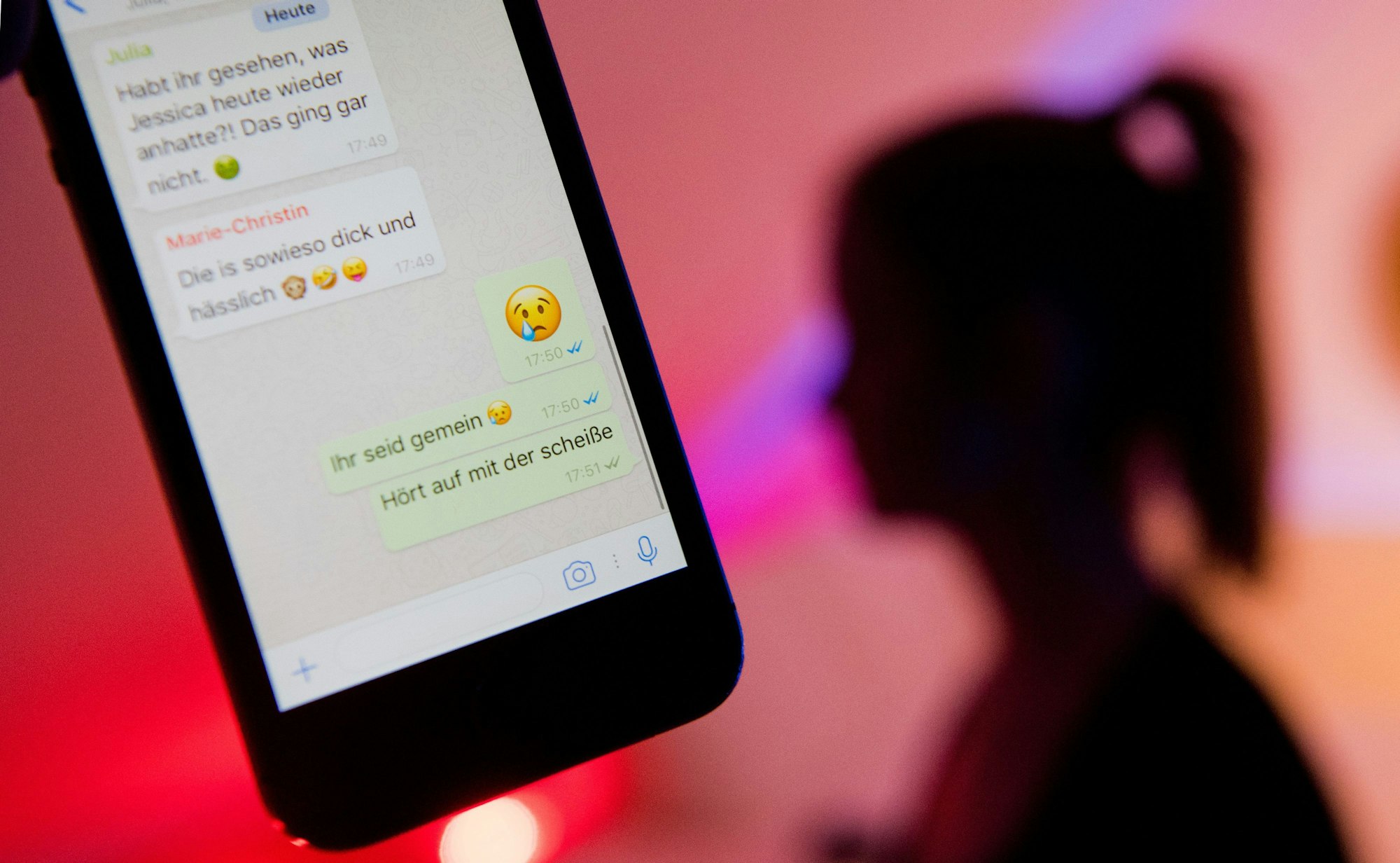 Jugendliche stehen massiv unter dem Eindruck aggressiver, unversöhnlicher Meinungskämpfe und persönlicher Angriffe in den sozialen Medien. Das Symbolbild zeigt Chat-Nachrichten auf einem Handy und die Silhouette eines Mädchens im Hintergrund.