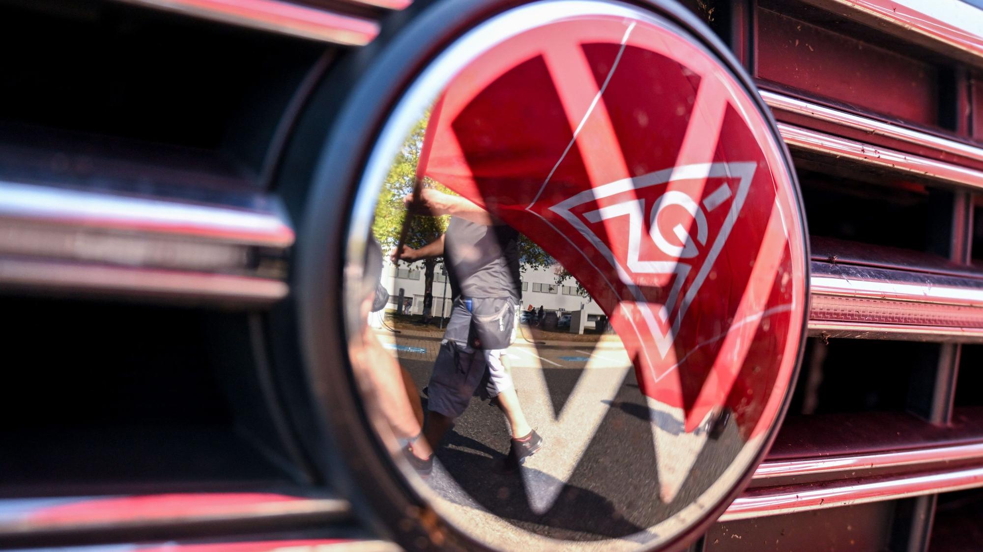 05.09.2024, Sachsen, Zwickau: Eine Fahne der IG Metall spiegelt sich in einem VW Logo. (zu dpa: «VW und IG Metall treffen sich zu zweiter Tarifrunde»)