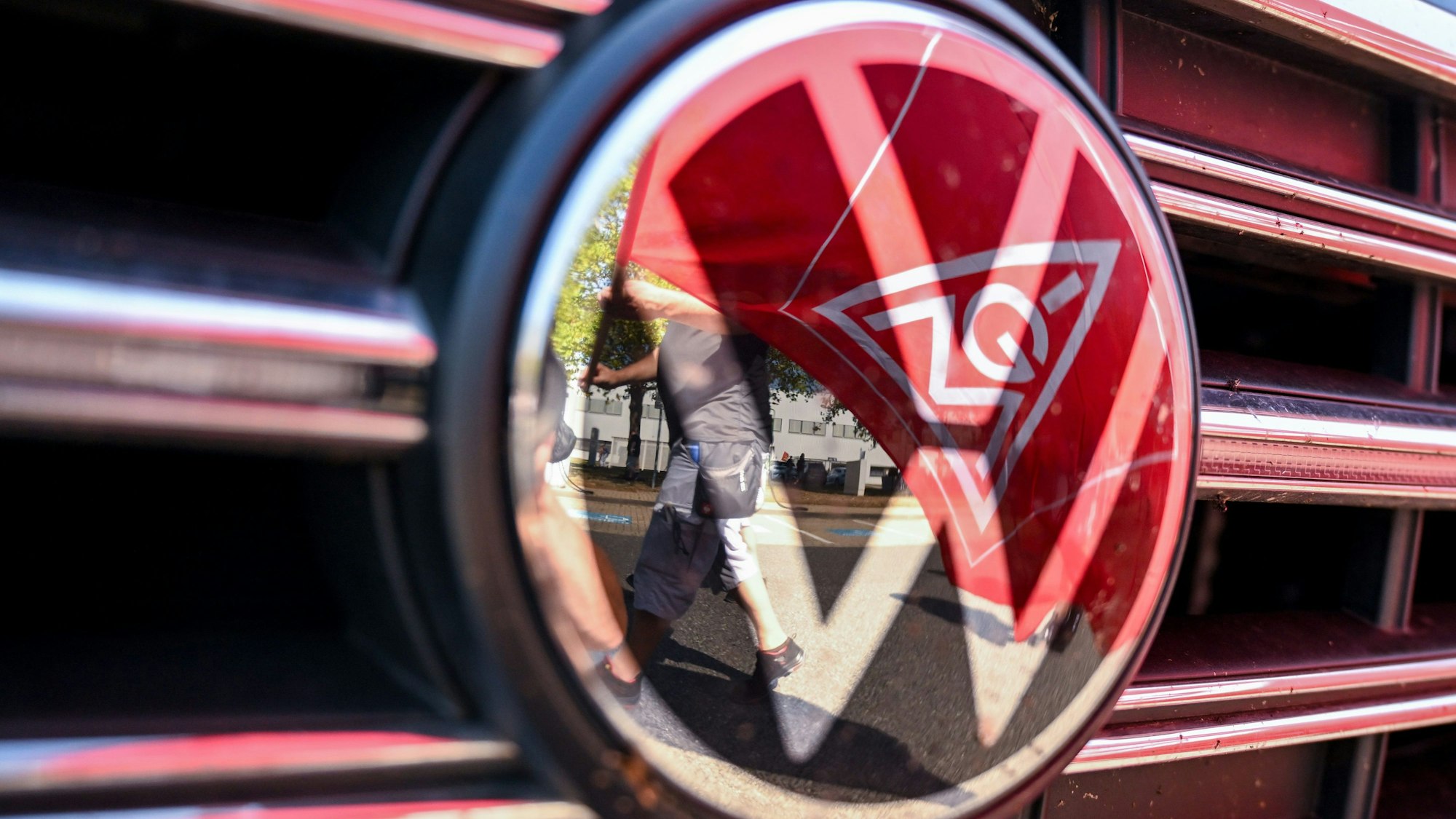 05.09.2024, Sachsen, Zwickau: Eine Fahne der IG Metall spiegelt sich in einem VW Logo. (zu dpa: «VW und IG Metall treffen sich zu zweiter Tarifrunde»)