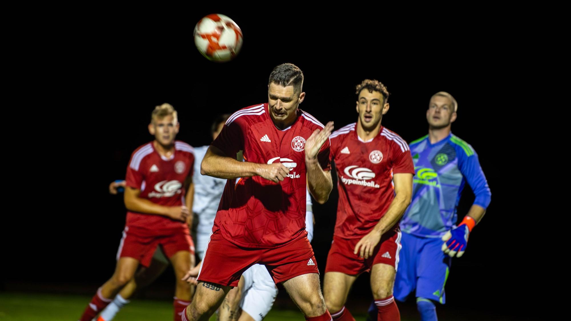 Ein Fußballer köpft einen Ball weg. Drei Mitspieler beobachten ihn dabei.