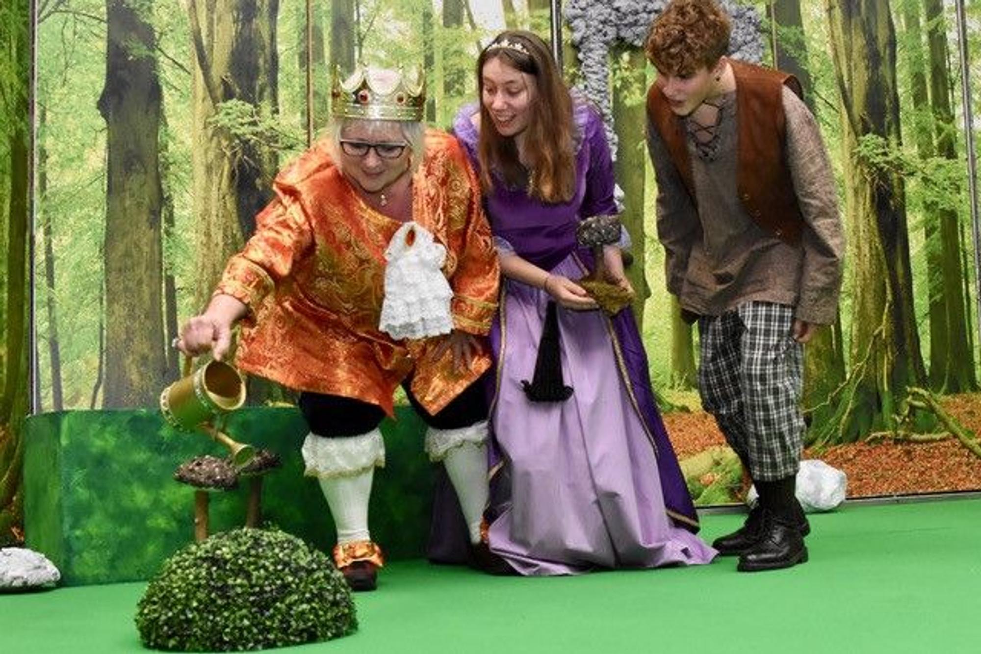 Drei Personen in Märchenkostümen auf einer Theaterbühne.