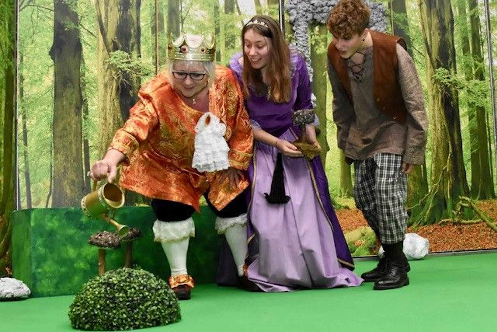 Drei Personen in Märchenkostümen auf einer Theaterbühne.