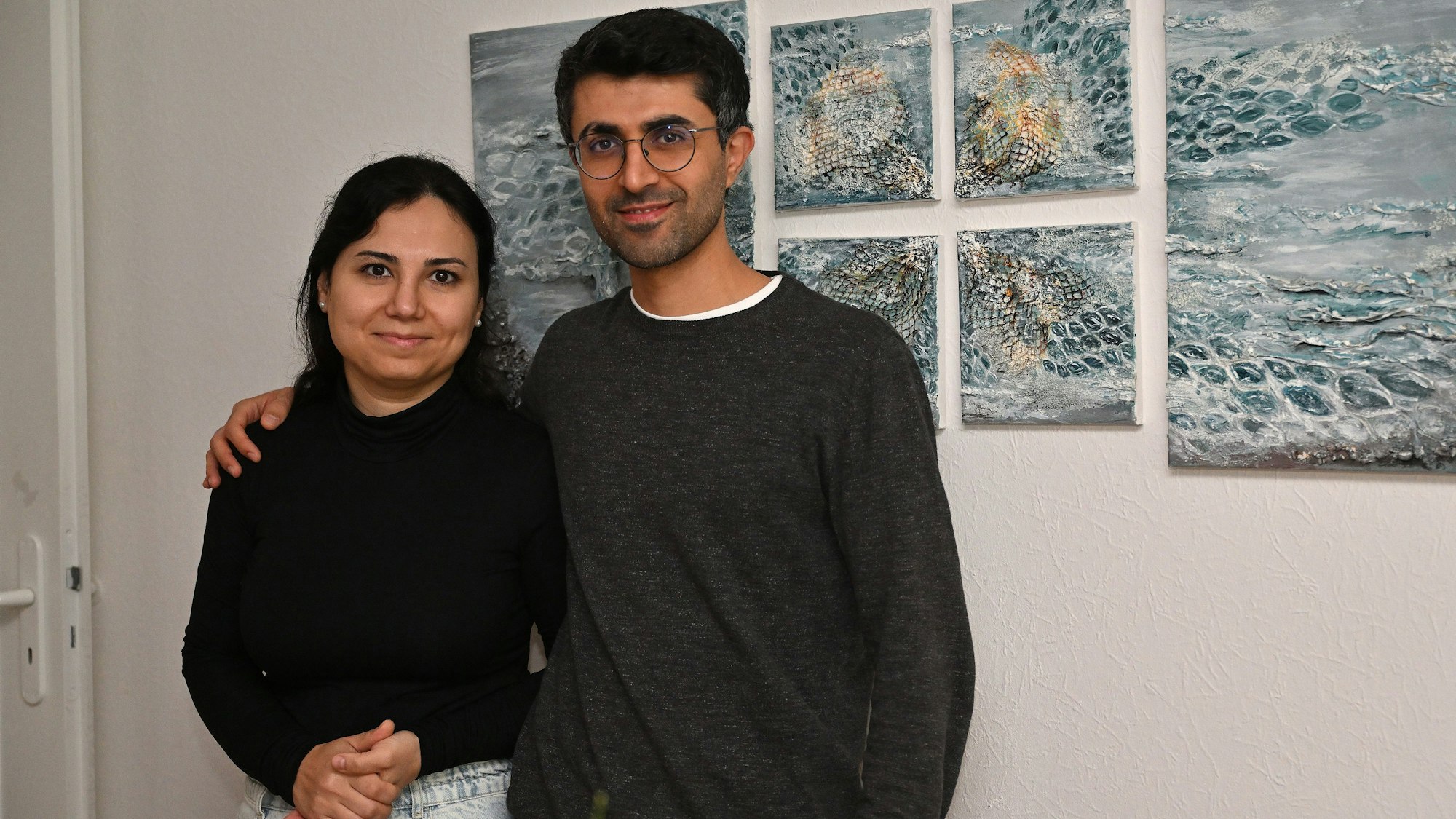 Das Ehepaar steht vor einem abstrakten Bild, das an der Wand hängt.