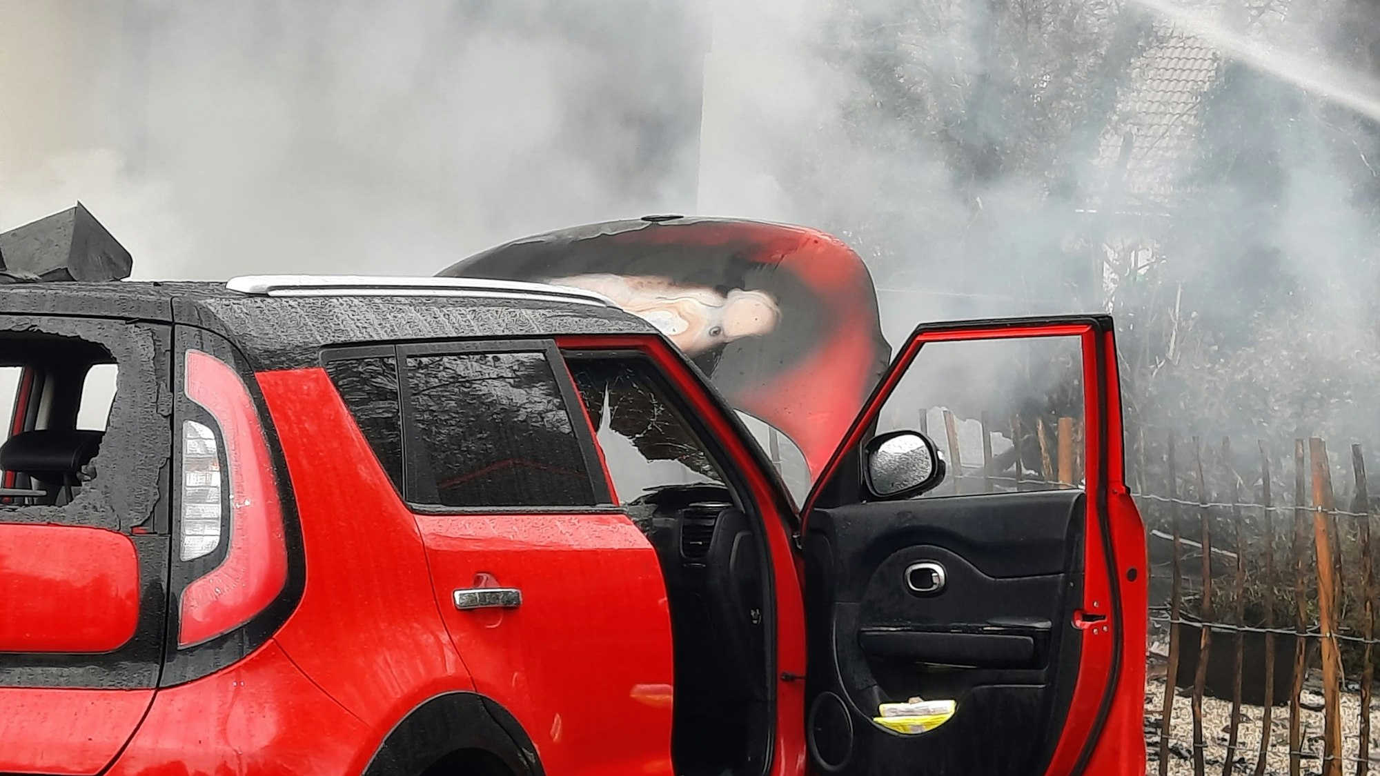 Ein roter Pkw mit offener Beifahrertür und mit Brandspuren.