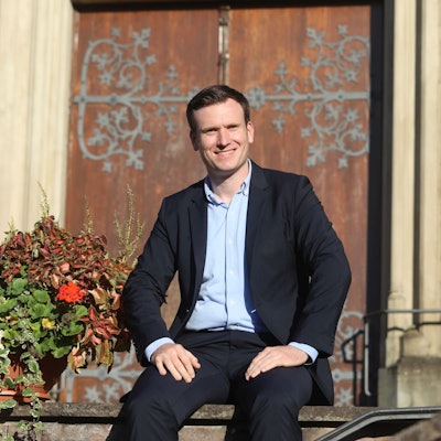 Ein Mann sitzt vor einer Kapelle mit einer schweren Holztür.