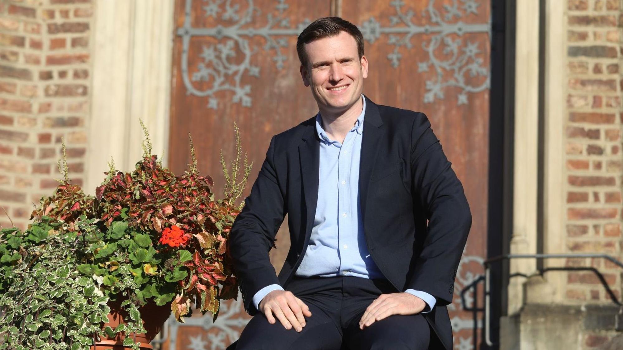 Ein Mann sitzt vor einer Kapelle mit einer schweren Holztür.