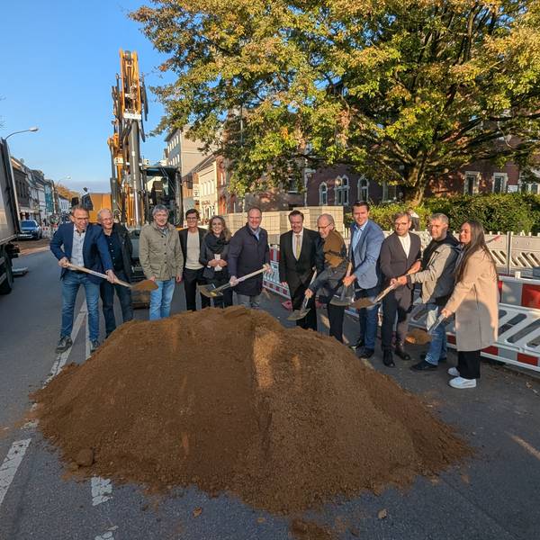 Das Foto zeigt eine Reihe von Menschen, die mit dem Spaten in einen Sandhaufen an der Baustelle auf der Luxemburger Straße stechen.