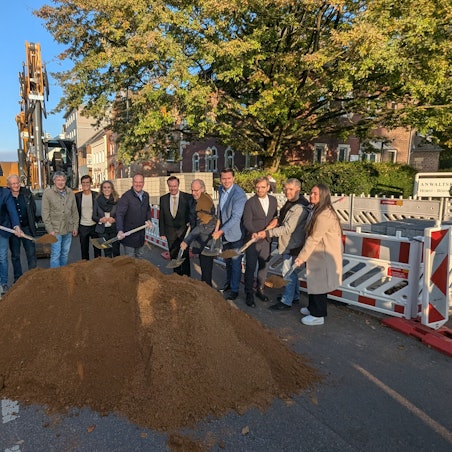 Das Foto zeigt eine Reihe von Menschen, die mit dem Spaten in einen Sandhaufen an der Baustelle auf der Luxemburger Straße stechen.
